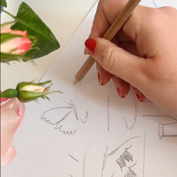 Zoom in of hand sketching on paper, drawing a butterfly framed by flowers