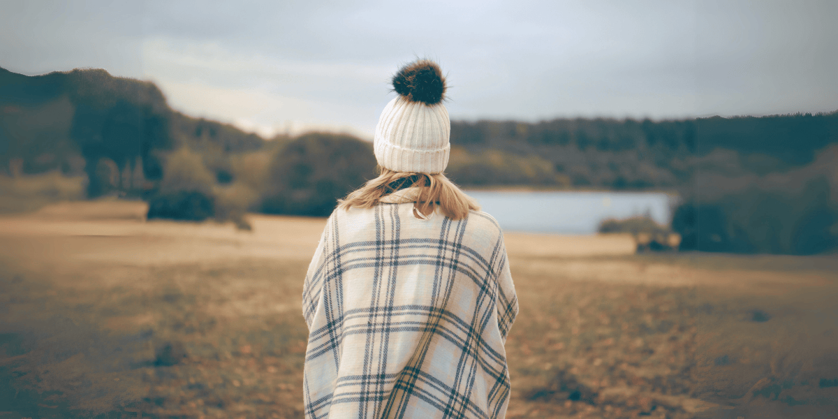 woman wearing a wolly hat in autum overlooking a lake.